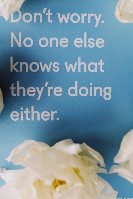 Close-up of a blue wall featuring white printed text that reads, 'Don't worry. No one else knows what they're doing either.' In the foreground, there are partially visible white flowers with soft, textured petals. The image emphasizes a motivational message, with no visible cleaning surfaces or tools present. This visual content is related to marketing or inspirational decor, and is associated with the domain deepcleaningmerton.co.uk, under the context of domestic cleaning and surface maintenance.